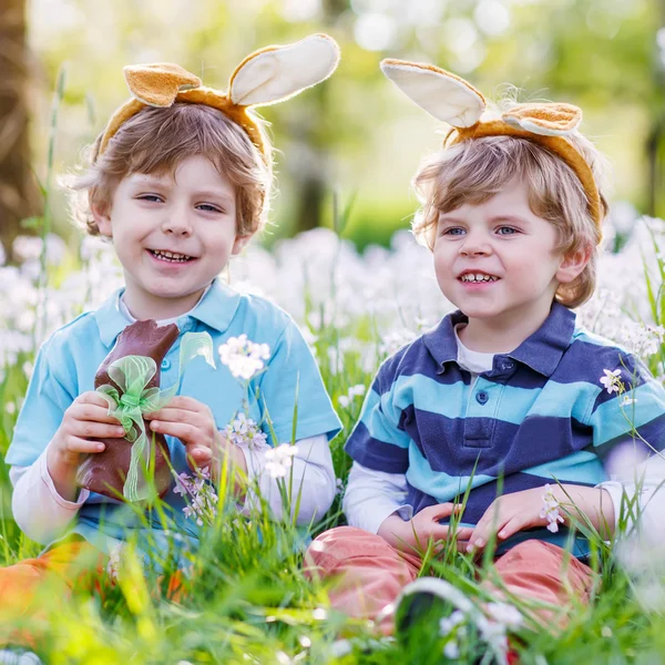 Dos niños pequeños usando orejas de conejo de Pascua y comiendo chocolate —  Fotos de Stock