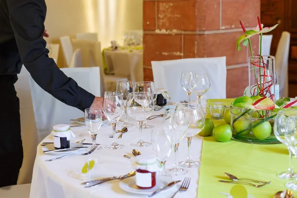 Waiter in black serving elegant table set in white and green — Stock Photo, Image