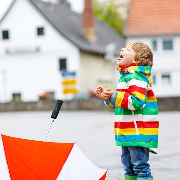Joyeux petit garçon souriant marchant en ville et jouant avec le rouge um — Photo