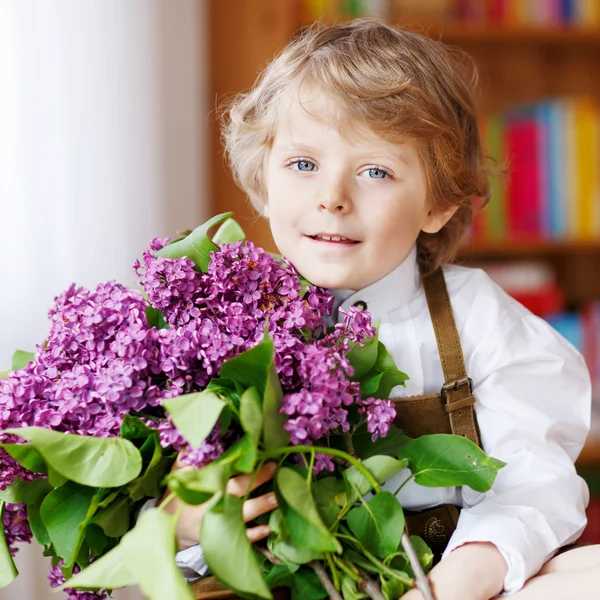 Αξιολάτρευτο χαμογελώντας λίγο αγόρι με ανθισμένα μοβ ιώδη λουλούδια — Φωτογραφία Αρχείου