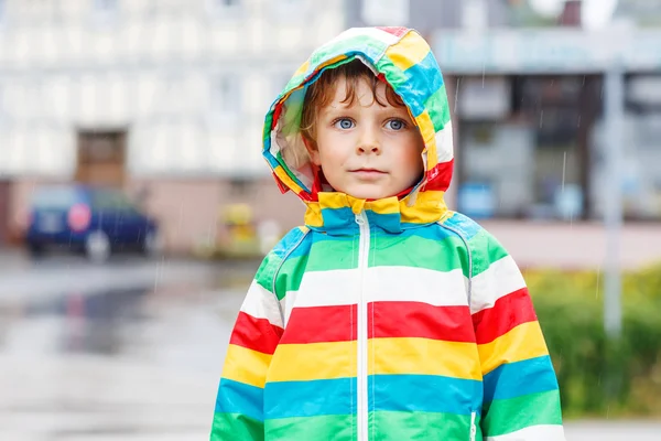 Glada leende liten pojke promenader i staden genom regn — Stockfoto