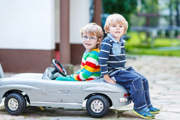 Two happy kids playing with big old toy car in summer garden, ou — Stock Photo, Image