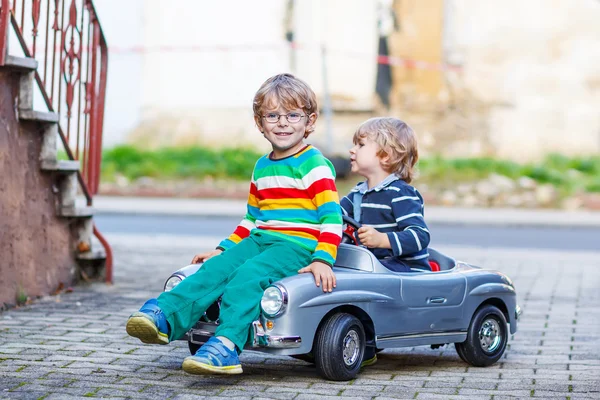 Två glada barn leker med stor gammal leksaksbil i sommar trädgård, ou — Stockfoto