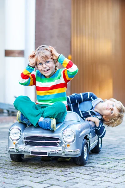 Två glada barn leker med stor gammal leksaksbil i sommar trädgård, ou — Stockfoto