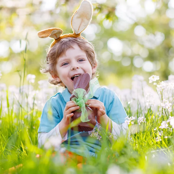 Kleines Kleinkind trägt Osterhasenohren und isst Schokolade lizenzfreie Stockfotos