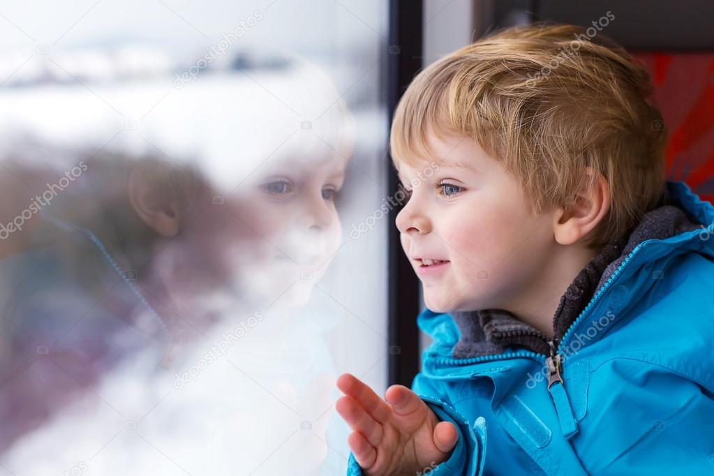 Beautiful toddler boy looking out train window outside and trave