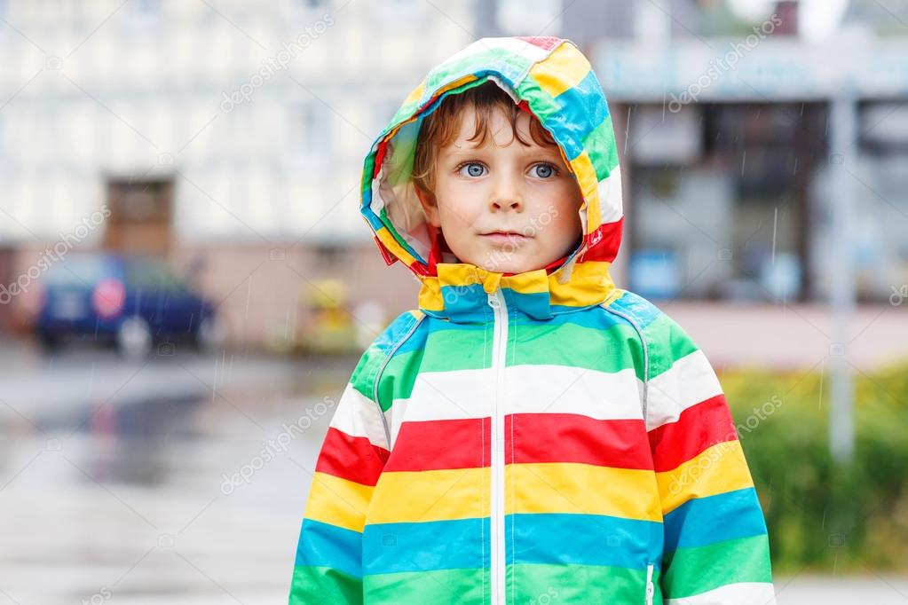 Happy smiling little boy walking in city through rain