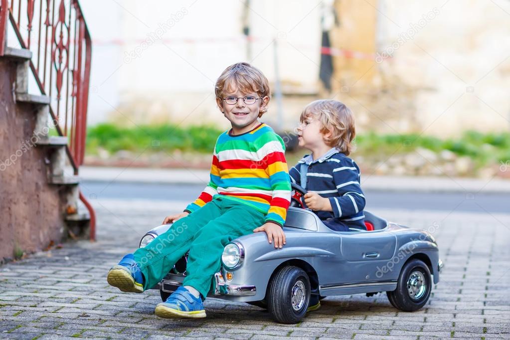 Two happy kids playing with big old toy car in summer garden, ou Stock