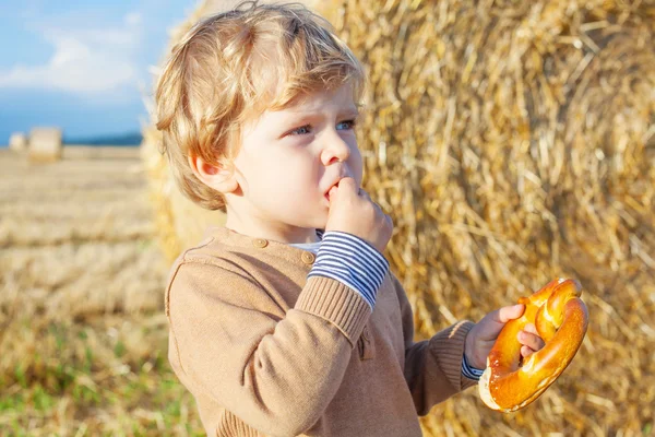 Funny cute little kid boy eating pretzel on late summer day on w — Stock Photo, Image