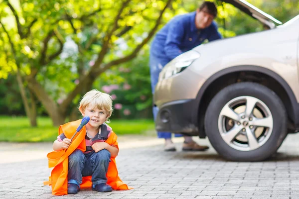 Petit garçon en gilet de sécurité orange pendant la réparation de son père fam — Photo