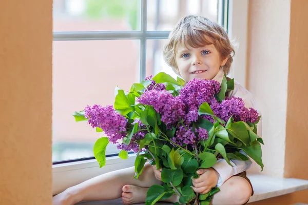Entzückend lächelnder kleiner Junge mit blühenden lila Fliederblumen — Stockfoto