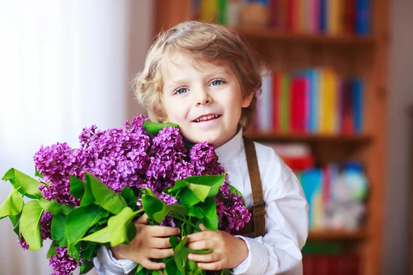 Entzückend lächelnder kleiner Junge mit blühenden lila Fliederblumen — Stockfoto