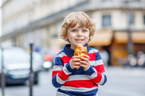 Маленький милый ребенок на улице города ест свежий круассан — стоковое фото