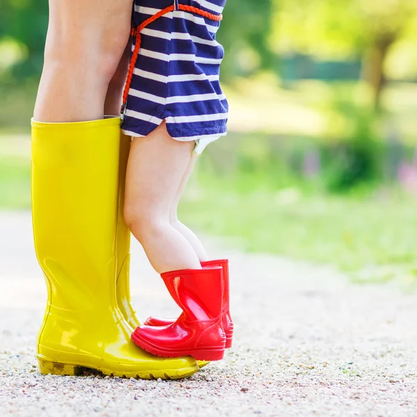 Benen på ung kvinna och hennes lilla tjej dotter i rainboots — Stockfoto