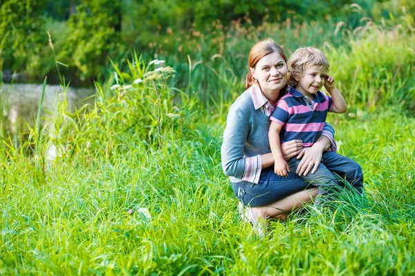 Menino e sua mãe sentados na grama na floresta de verão — Fotografia de Stock