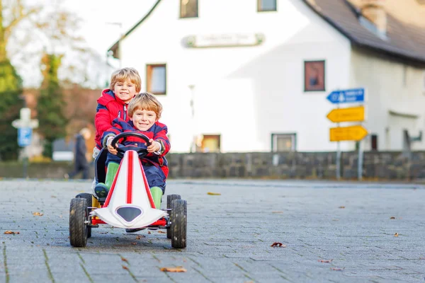 Due piccoli amici bambini in giacche rosse guida veloce auto da corsa insieme — Foto Stock