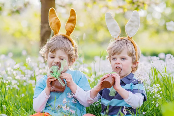 İki küçük arkadaş Paskalya bunny kulaklar ve yeme çikolata ile — Stok fotoğraf