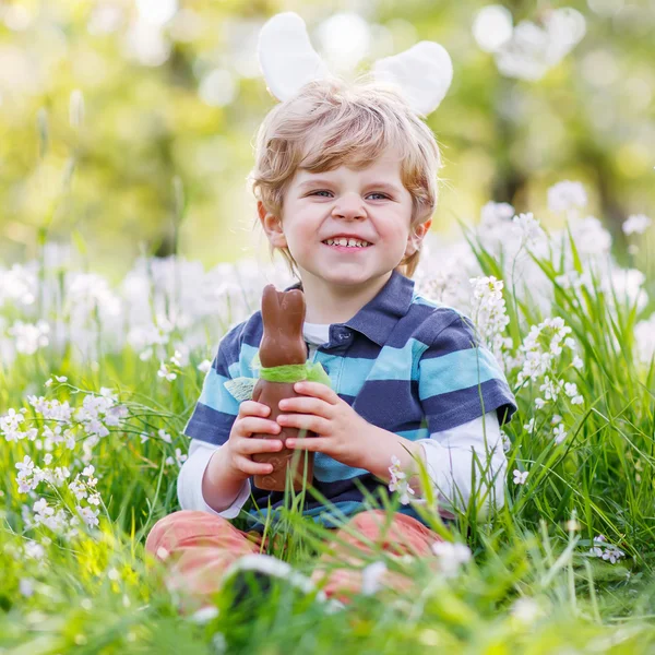 Pequeño niño con orejas de conejo de Pascua y comer chocolate en —  Fotos de Stock