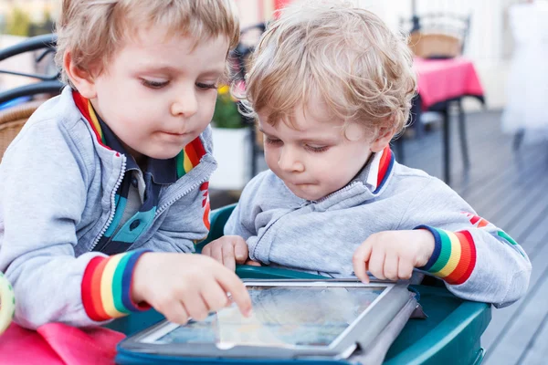 Два маленьких сидящих мальчика веселятся вместе с планшетным компьютером . — стоковое фото