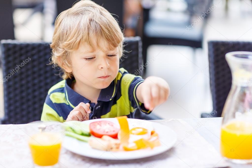 Little kid boy having healthy breakfast in hotel restaurant or c