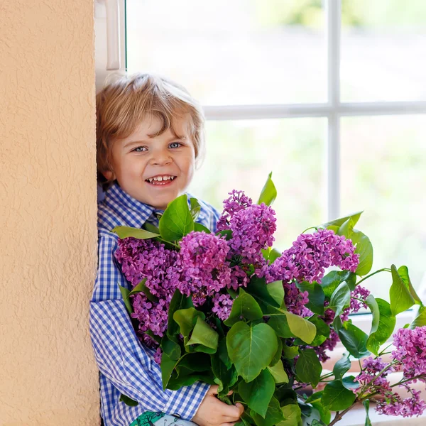 Очаровательный улыбающийся маленький мальчик с цветущими фиолетовыми сиреневыми цветами — стоковое фото