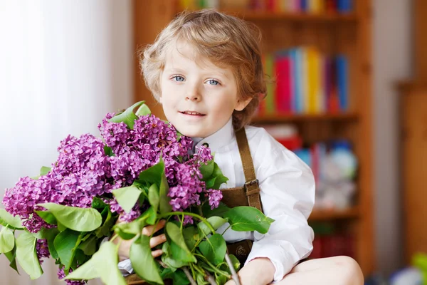 Menino sorridente adorável com flores lilás roxas florescendo — Fotografia de Stock