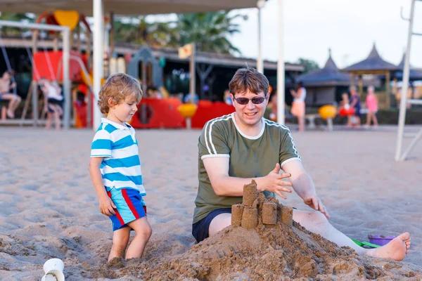 Pai feliz e filho pequeno construindo castelo de areia em bea de areia — Fotografia de Stock