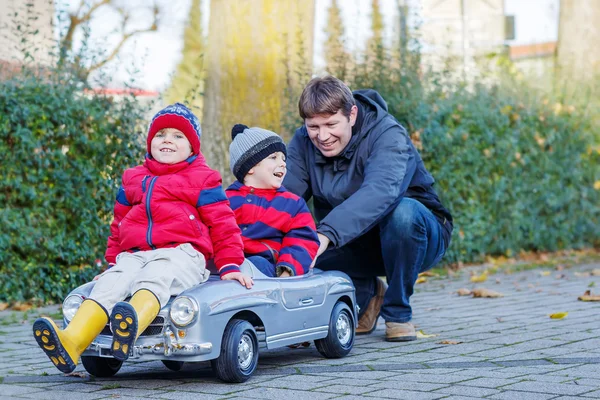 Två glada syskon pojkar och pappa leker med stor gammal leksaksbil, — Stockfoto