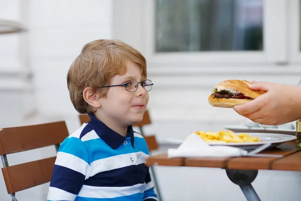 Malý chlapec jíst fast food: hranolky a hamburger — Stock fotografie