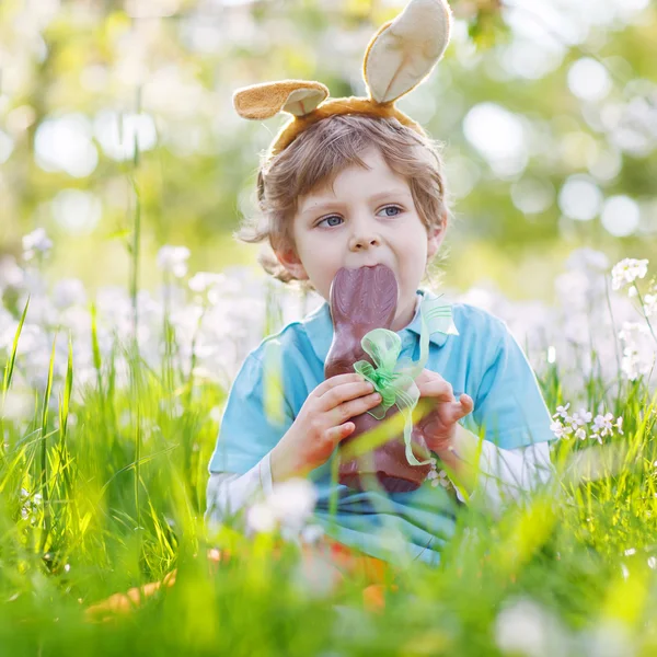 Kleines Kind trägt Osterhasenohren und isst Schokolade — Stockfoto