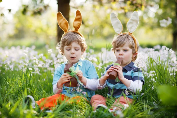 Два маленьких мальчика с пасхальными ушами и едят шоколад. — стоковое фото
