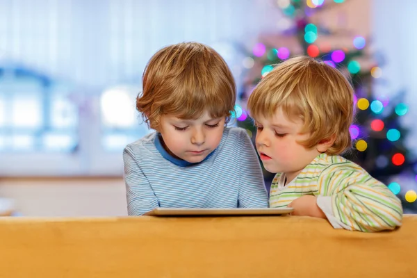 Duas crianças pequenas felizes brincando com tablet pc, dentro de casa — Fotografia de Stock