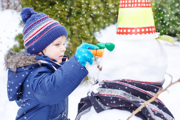 Adorable niño divirtiéndose con muñeco de nieve en el día de invierno — Foto de Stock