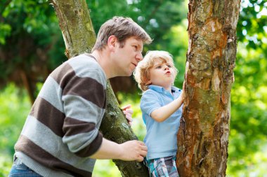 Cute little kid boy enjoying climbing on tree with father, outdo clipart