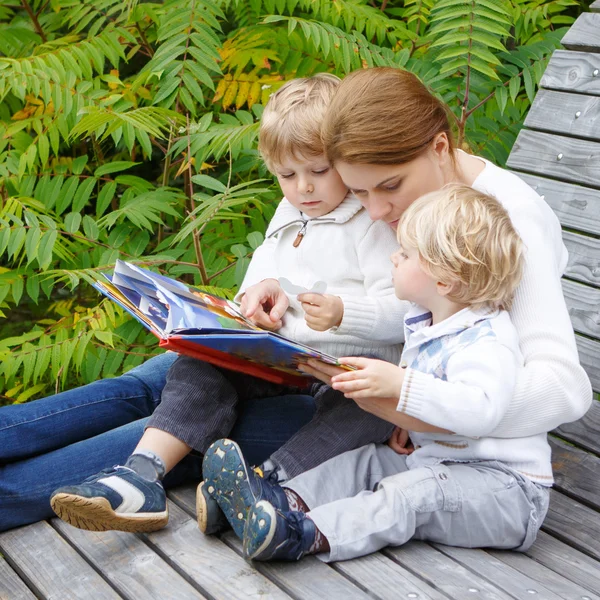 Frau und zwei kleine Geschwister sitzen auf Bank im Park und lesen — Stockfoto