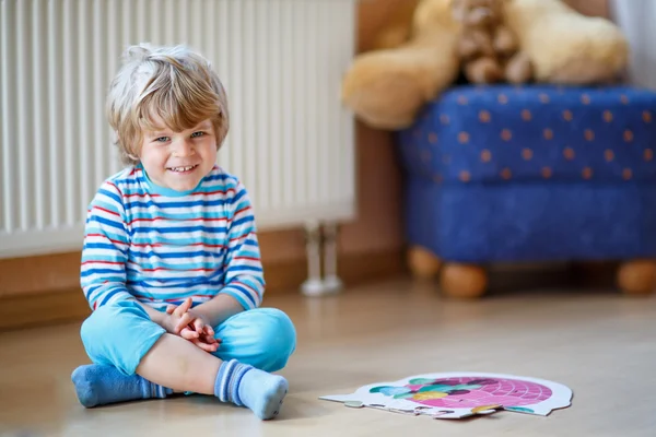 Piccolo ragazzo biondo carino che gioca con puzzle game a casa — Foto Stock