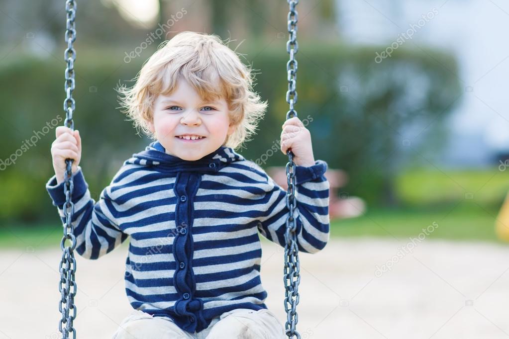 Adorable toddler boy having fun chain swing on outdoor playgroun