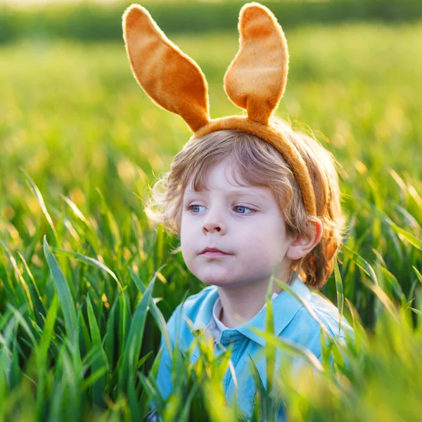 Lindo niño pequeño con orejas de conejo de Pascua jugando en hierba verde —  Fotos de Stock