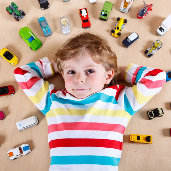 Pequeño niño rubio jugando con un montón de coches de juguete en interiores —  Fotos de Stock