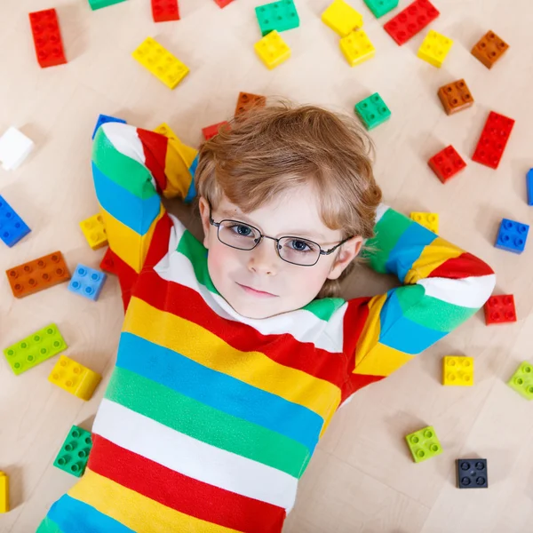 Piccolo ragazzo biondo che gioca con un sacco di blocchi di plastica colorati — Foto Stock