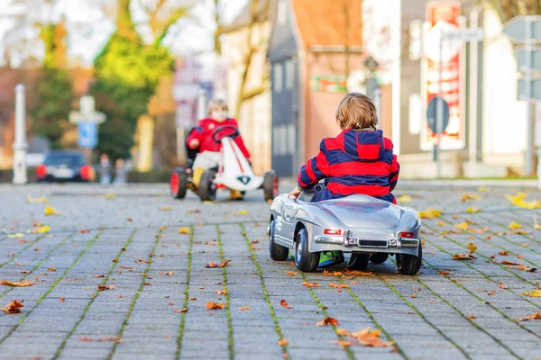 Dos niños pequeños con chaquetas rojas que conducen viejos coches vintage y de carreras —  Fotos de Stock