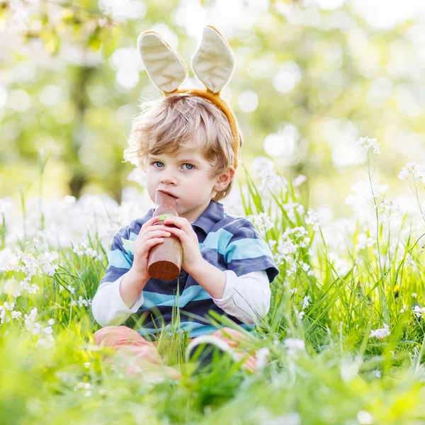 Divertido niño con orejas de conejo de Pascua y comer chocolate en sp — Foto de Stock