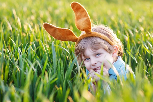 Entzückender kleiner Junge mit Osterhasenohren, der im grünen Gras spielt — Stockfoto