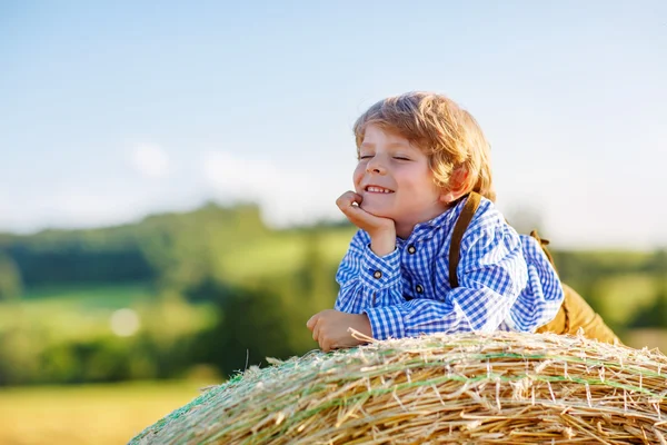 Funny little kid boy lying on hay stack  and smiling — Stock Photo, Image