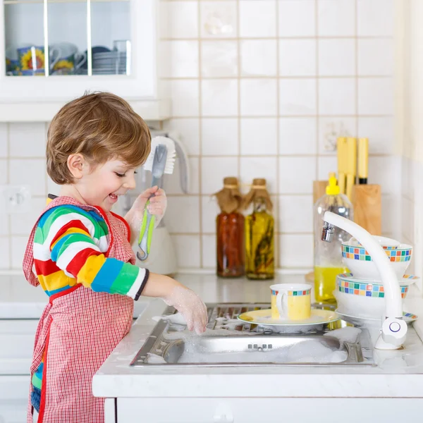Glücklicher kleiner blonder Junge beim Geschirrspülen in der heimischen Küche — Stockfoto