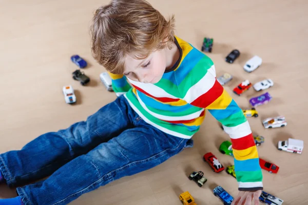 Pequena criança loira brincando com muitos carros de brinquedo interior — Fotografia de Stock