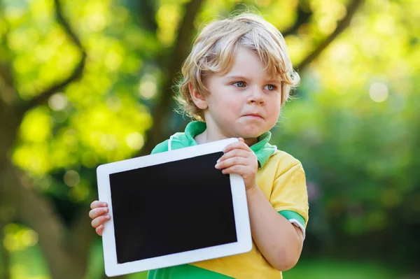 Adorabile bambino confuso che tiene in mano tablet pc, all'aperto — Foto Stock