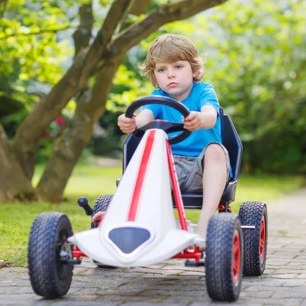 Pequeño niño activo que se divierte y conduce coche de carreras de juguetes — Foto de Stock
