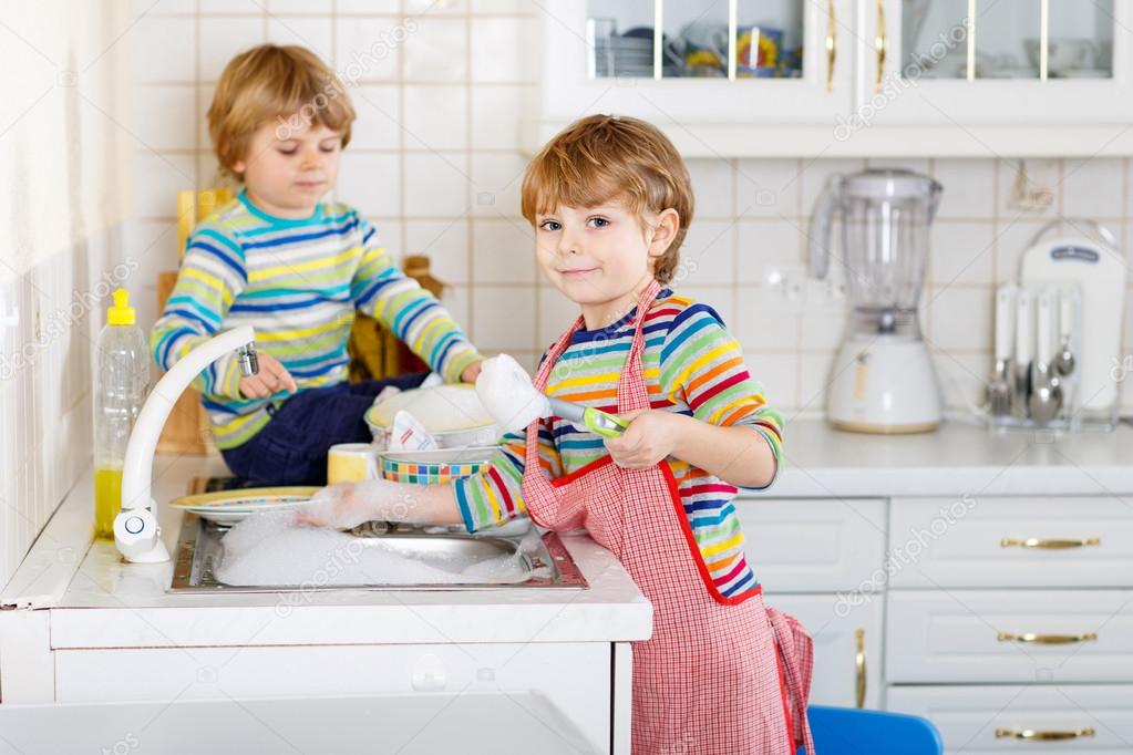 Two funny little boy friends washing dishes in domestic kitchen