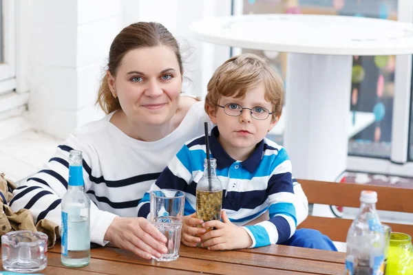 Little boy with glasses and his mother enjoying drinks